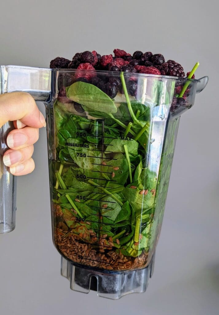 Vitamix blender filled with flax seeds, spinach, banana, and frozen mixed berries ready to make blood sugar-friendly smoothie