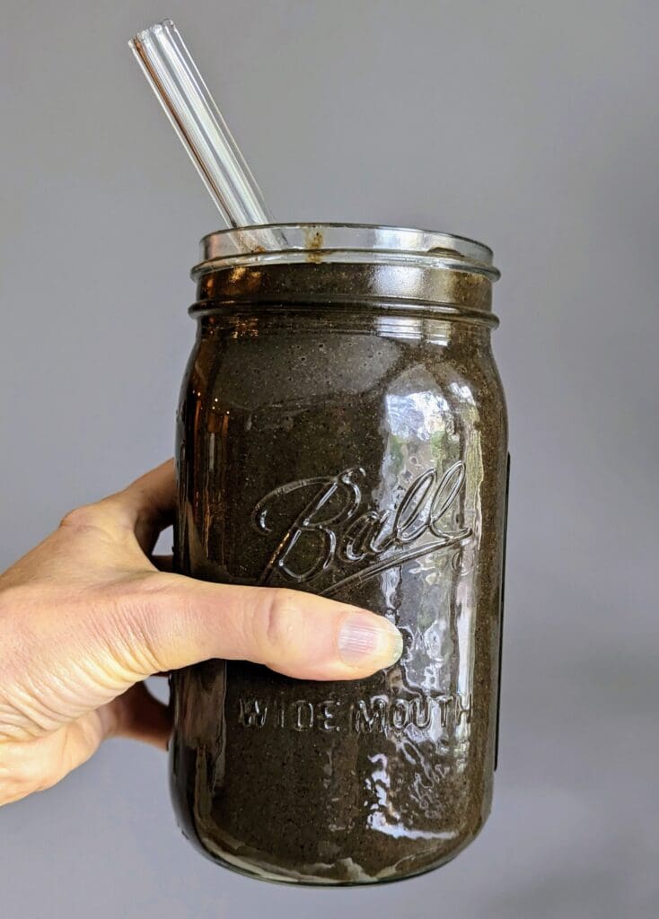 Hand holding green whole food smoothie in Ball mason jar with glass straw, showing final blended result of blood sugar-friendly smoothie recipe
