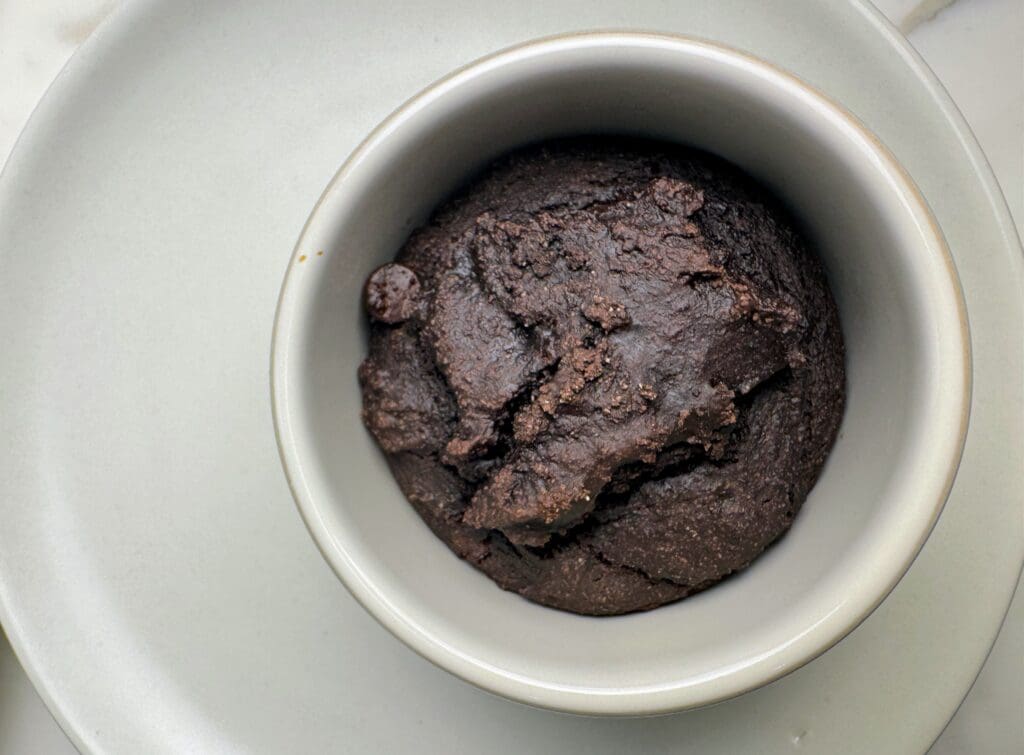 Plant-based chocolate mug cake in white ceramic ramekin showing dense, fudgy texture made with whole grain flour and cacao powder