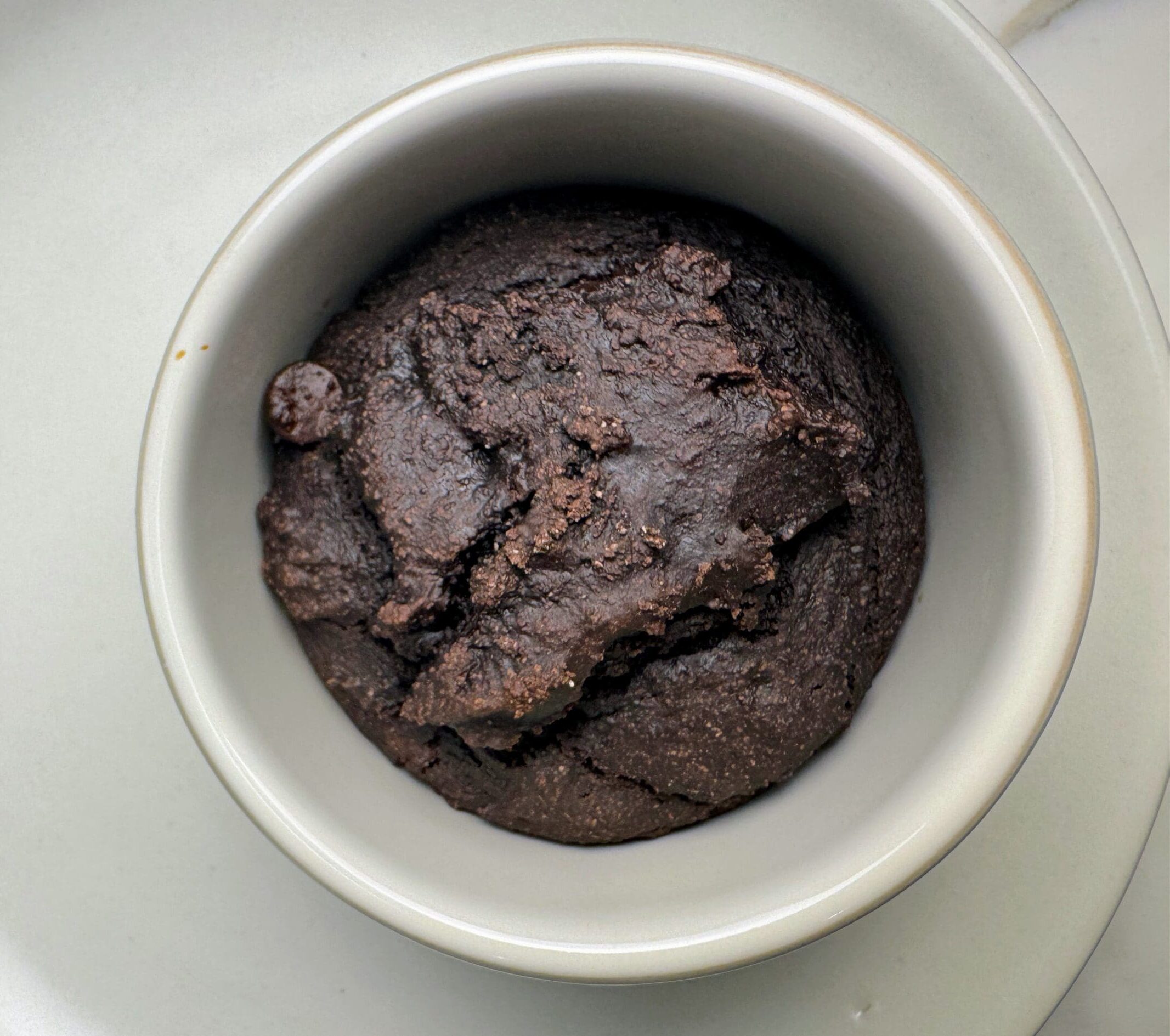 Plant-based chocolate mug cake in white ceramic mug showing dense, fudgy texture made with whole grain flour and cacao powder