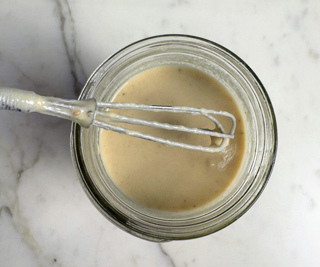 Homemade lemon tahini salad dressing in glass jar with whisk, oil-free wellness retreat recipe