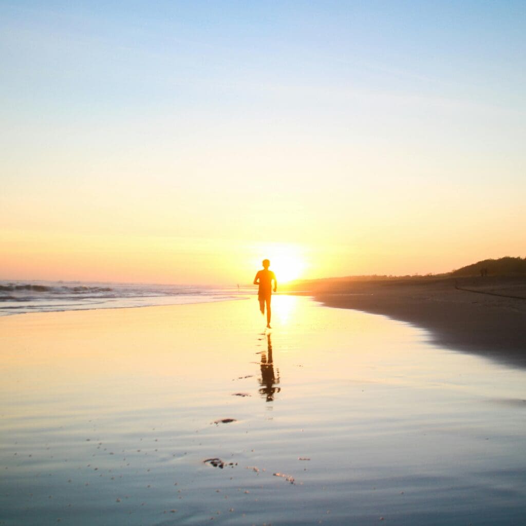 Person running on beach at sunset with golden sunlight reflecting on wet sand