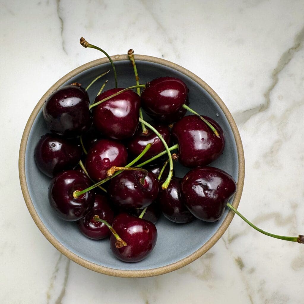 Bowl of fresh dark red cherries with stems on marble countertop