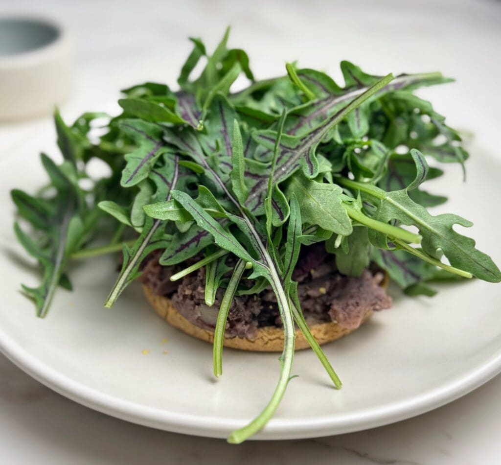 Buckwheat English muffin topped with black beans and fresh wild arugula on white plate representing heart-healthy plant-based nutrition