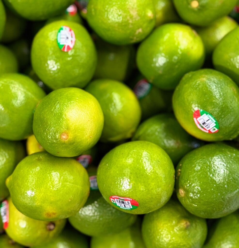 Fresh green limes with produce stickers at grocery store, showing the first step in creating homemade electrolyte lime water