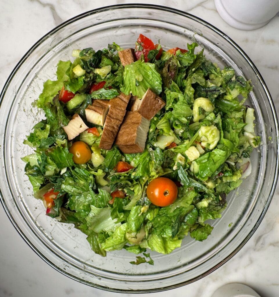 Nutrient-dense salad with cubed baked tofu, mixed greens, cherry tomatoes, and diverse vegetables in large glass mixing bowl
