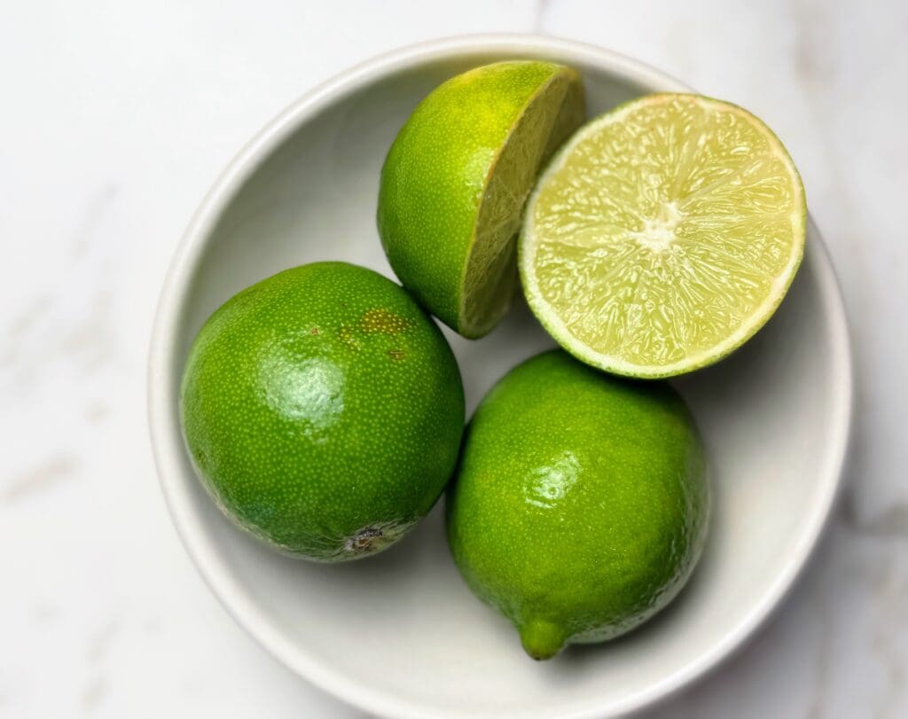 Fresh limes cut in half in white bowl showing juicy interior, demonstrating the key ingredient for lime water recipe