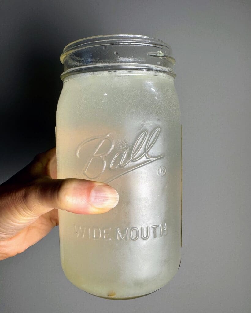 Hand holding Ball mason jar filled with clear lime water drink, showing the final homemade electrolyte beverage