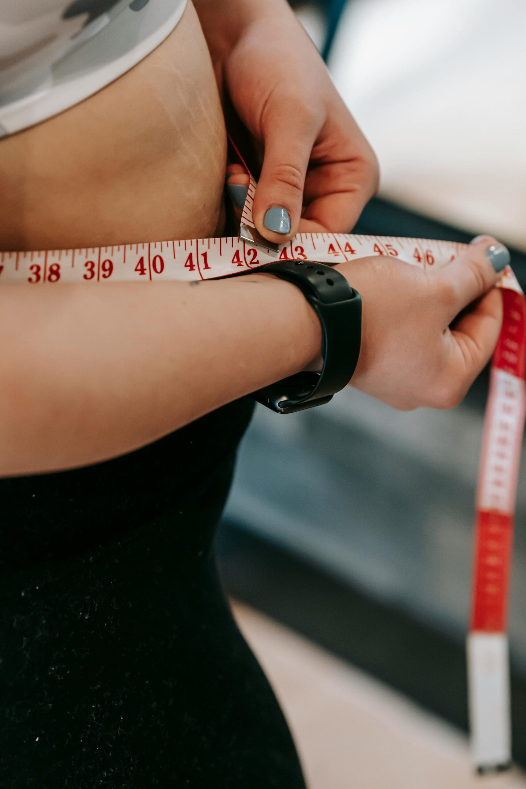 Person measuring waist circumference with measuring tape while wearing fitness tracker, demonstrating simple method to assess visceral fat risk