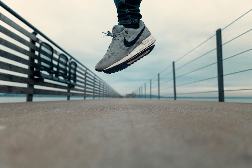 Close-up of person's feet in gray sneakers jumping on outdoor walkway for bone health exercise
