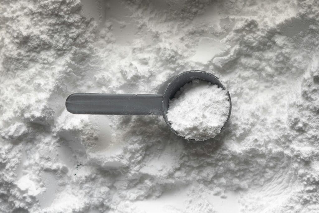 Measuring scoop filled with white creatine powder against textured background