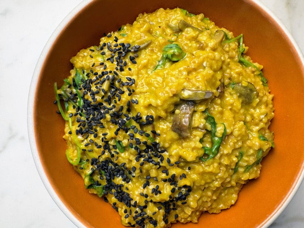 Savory steel cut oats with kale, artichokes, mushrooms and black sesame seeds in orange bowl