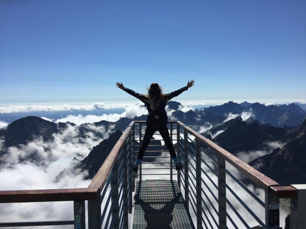 Person standing with arms raised on mountain observation platform above clouds, representing optimal health and extended healthspan