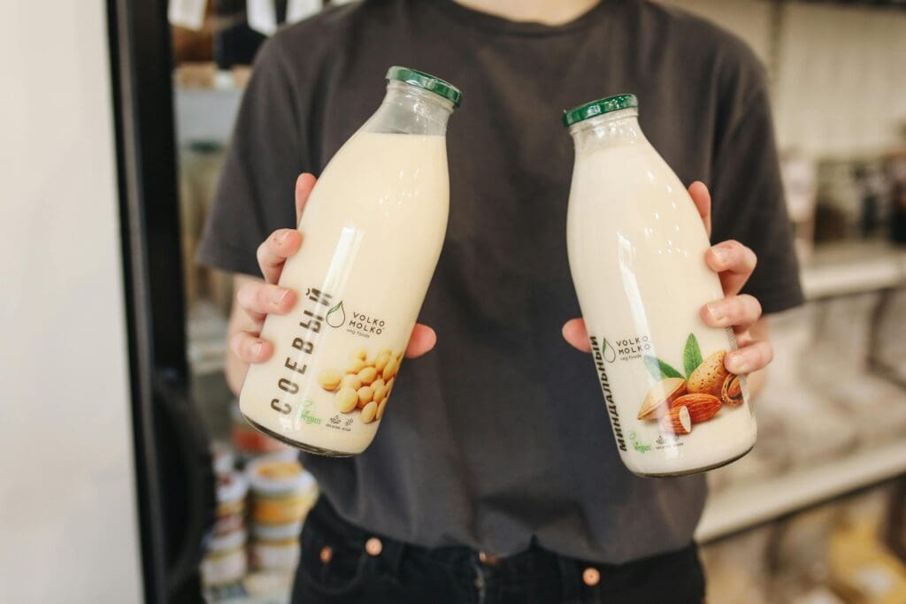 Person holding bottles of soy milk and almond milk in grocery store showing plant milk comparison
