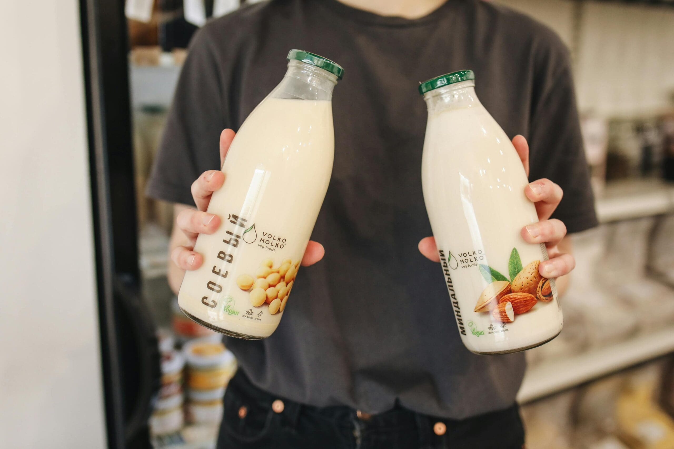 Person holding bottles of soy milk and almond milk in grocery store showing plant milk comparison
