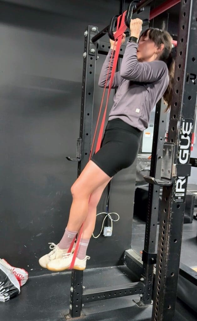 Woman performing assisted pull-up at gym showing resistance training at 53