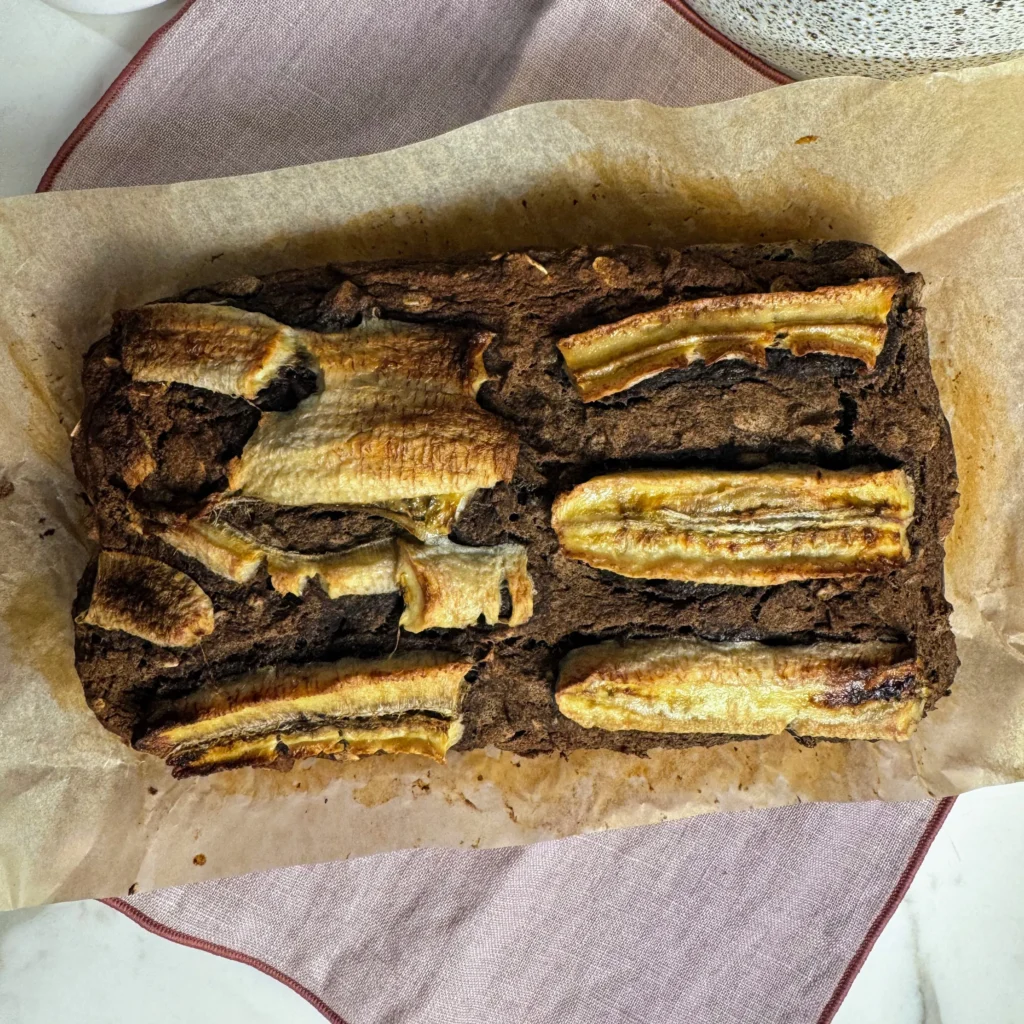 Homemade banana bread in a parchment-lined loaf pan, topped with caramelized banana slices