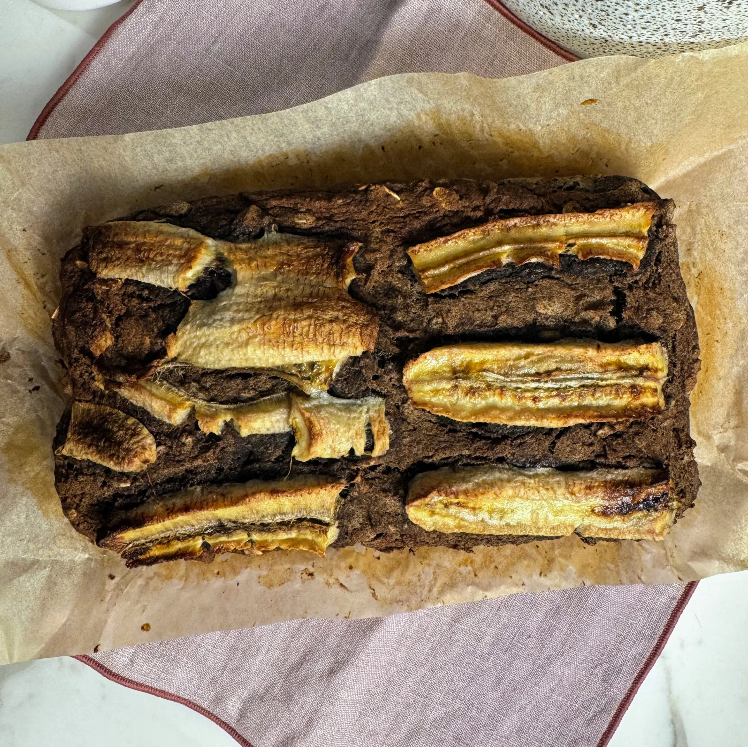 Homemade banana bread in a parchment-lined loaf pan, topped with caramelized banana slices